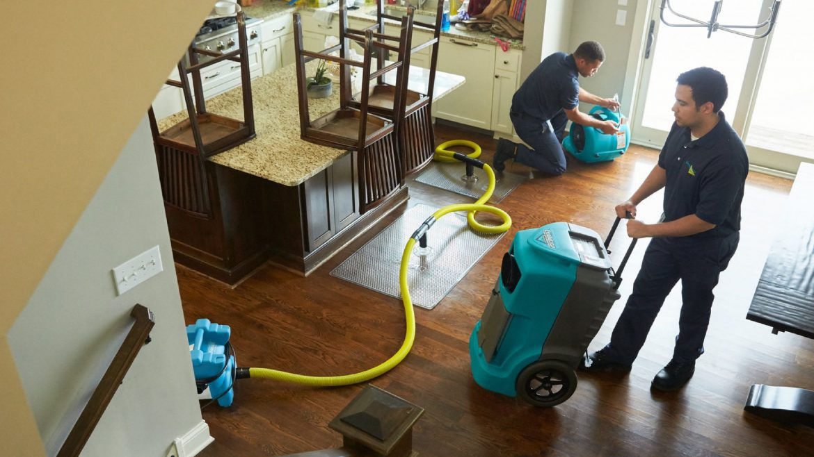 Two technicians use industrial water extraction equipment in a flooded kitchen,