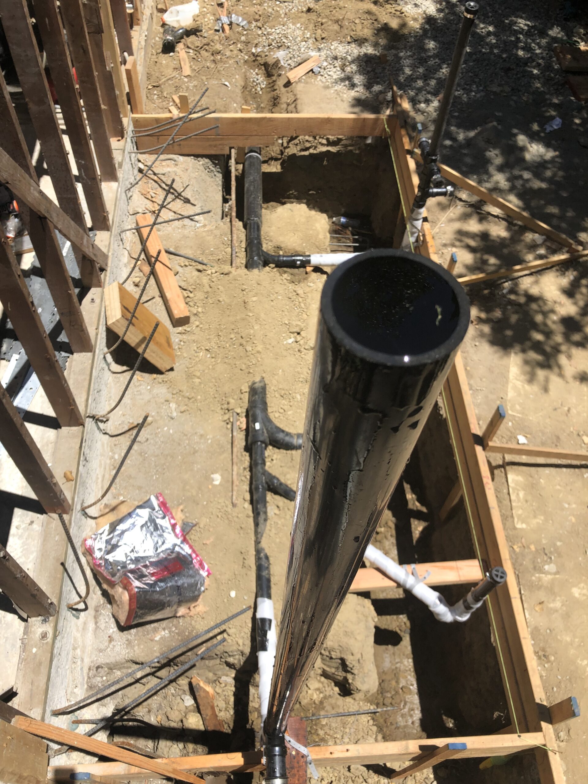 Construction site featuring a vertical black pipe emerging from a dirt foundation