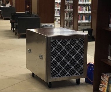 Mobile air purifier on wheels, positioned in a library setting.